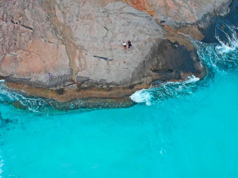 fotografía aérea de una pareja estirada en una roca y el mar